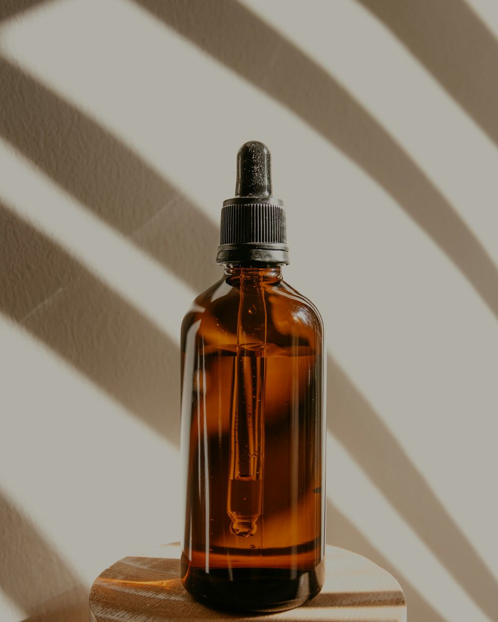 Amber glass dropper bottle on a wooden block, crossed by leaf shadows