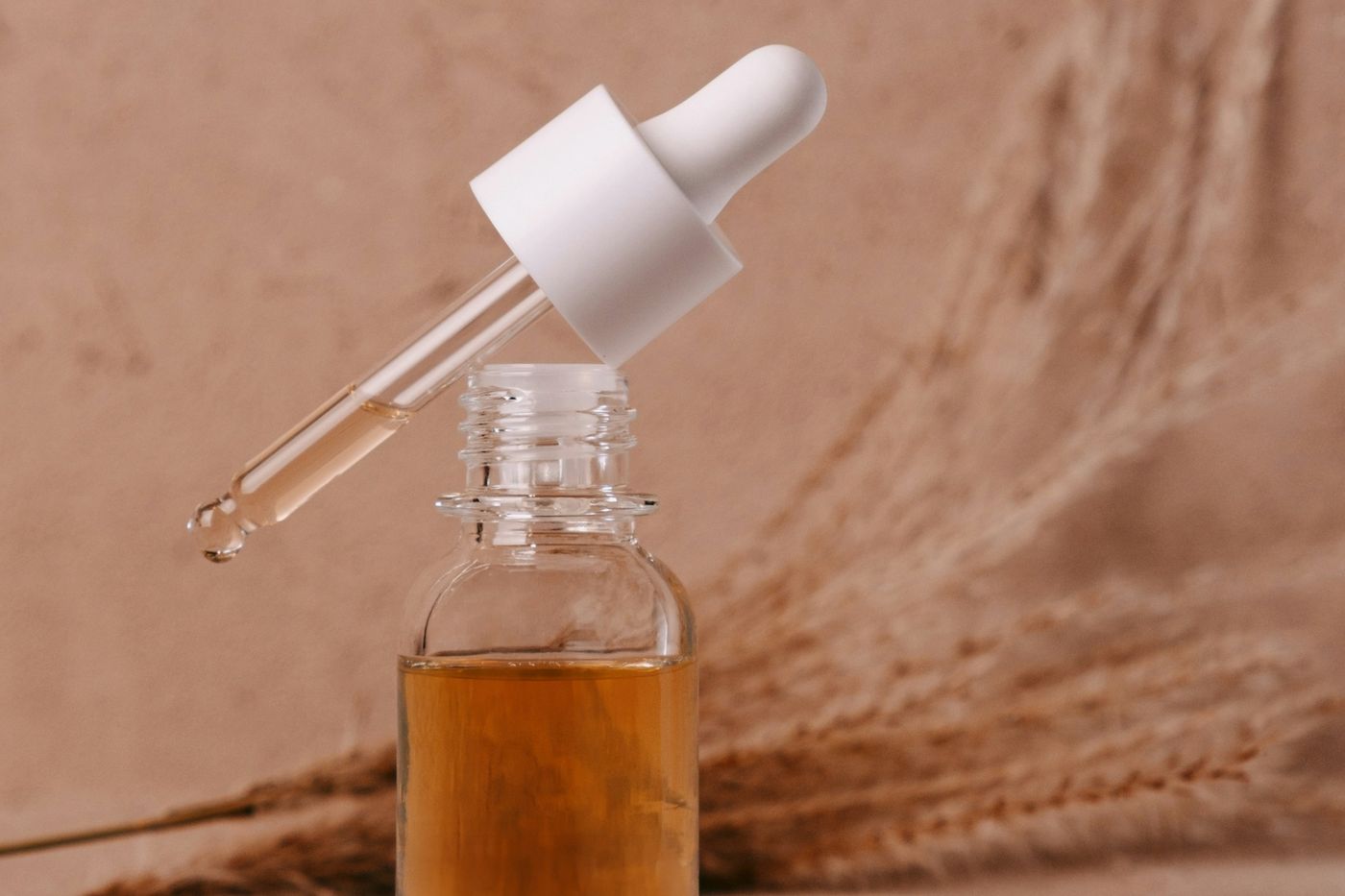 Amber serum in a glass dropper bottle beside dried grasses