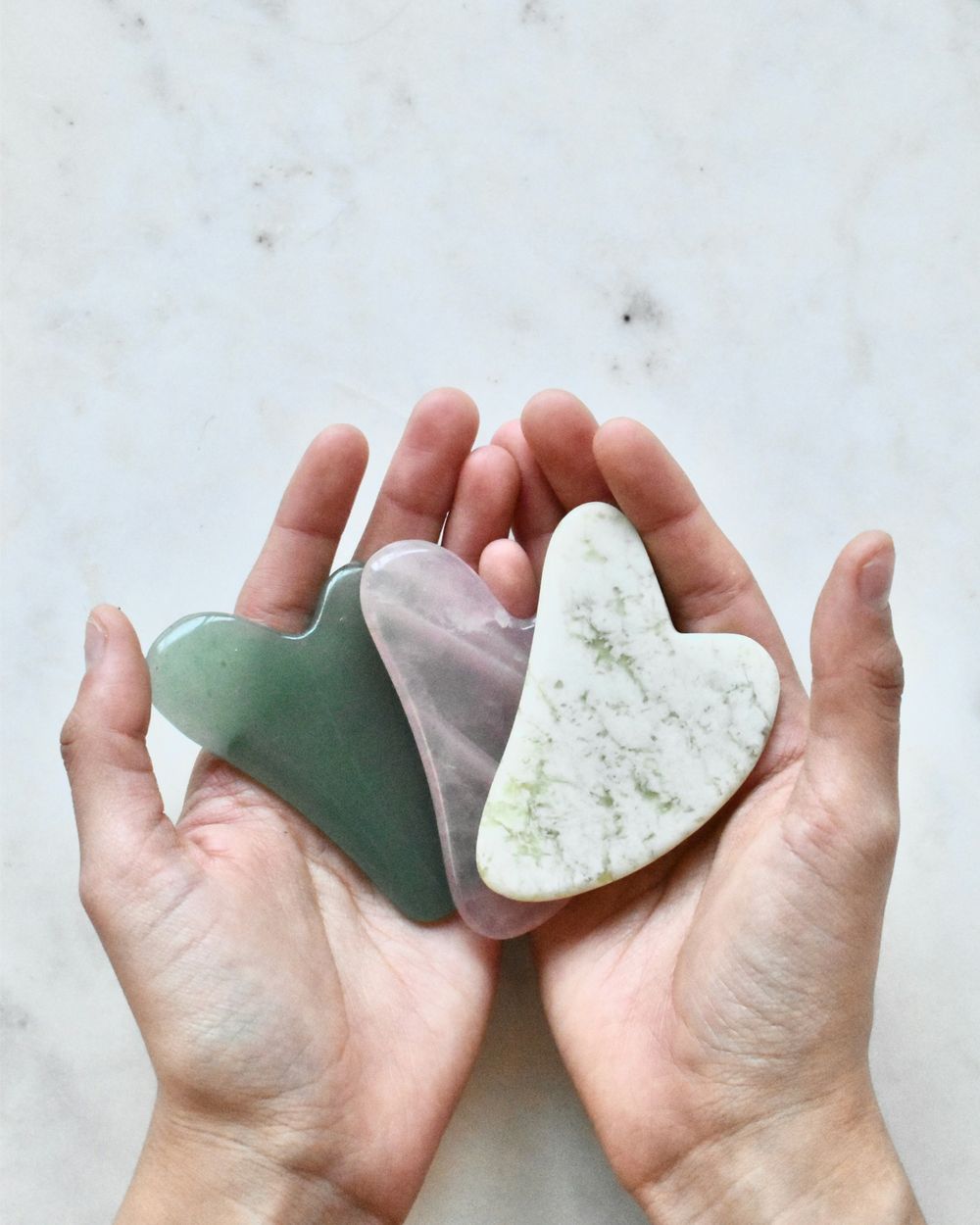 Open hands holding heart-shaped facial massage stones