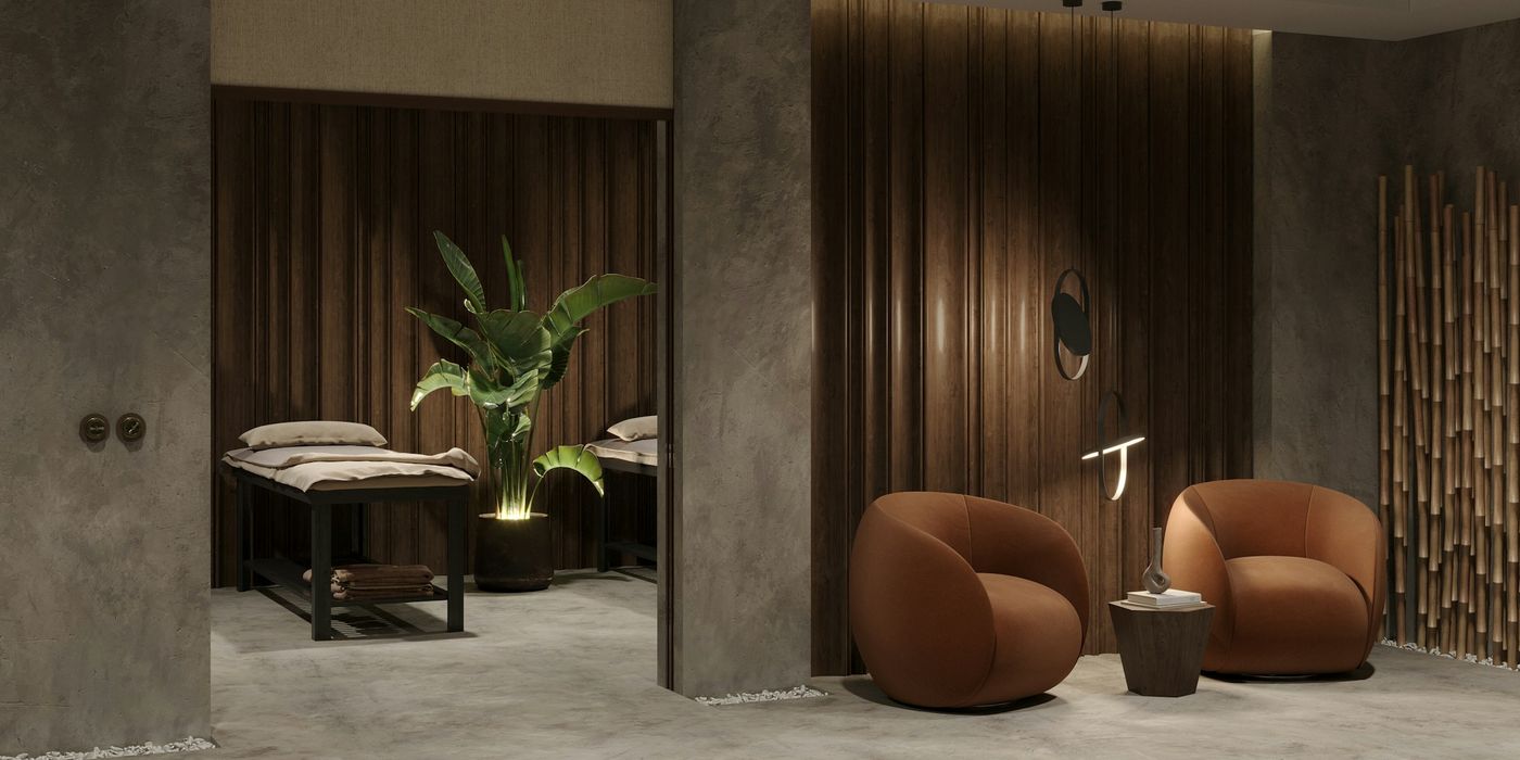 Calm treatment room with a massage bed, a tall plant and two rounded armchairs in warm, low light